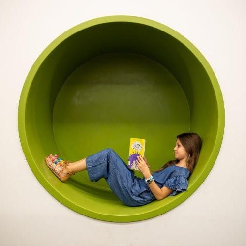 A girl reading a book while reclining in a green circular nook.