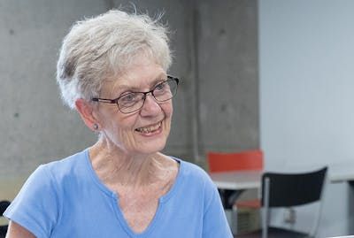 Woman with short white hair and glasses is looking to the right and smiling